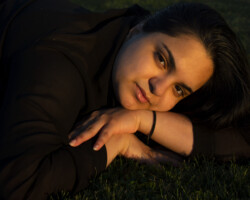 <Img alt=" A portrait of a model laying down on grass during golden hour">